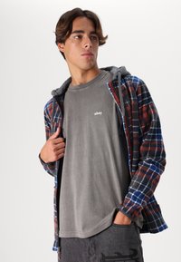 Red, blue, and black checkered flannel jacket with a gray hood, layered over a fitted gray shirt displaying "obey" logo on the chest.