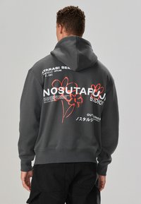 Felpa grigia con cappuccio e tasca a marsupio, con scritte grafiche bianche e rosse e motivi floreali sul retro. Tessuto morbido con polsini a coste.