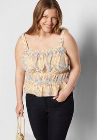 Top peplum com padrão de gingham nas tonalidades amarela, laranja e teal; apresenta alças ajustáveis e cintura elástica com franzido. Jeans de ganga escura.