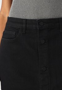 Fustă din denim negru cu talie ajustată, având cinci butoane frontale, două buzunare laterale și o textură fină. Top gri cu dungi deasupra.