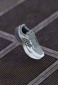 Jasnoszary but do biegania z siateczkową cholewką, wyściółką podeszwy i czarnymi akcentami logo. Charakteryzuje się smukłym designem i teksturowanymi detalami.