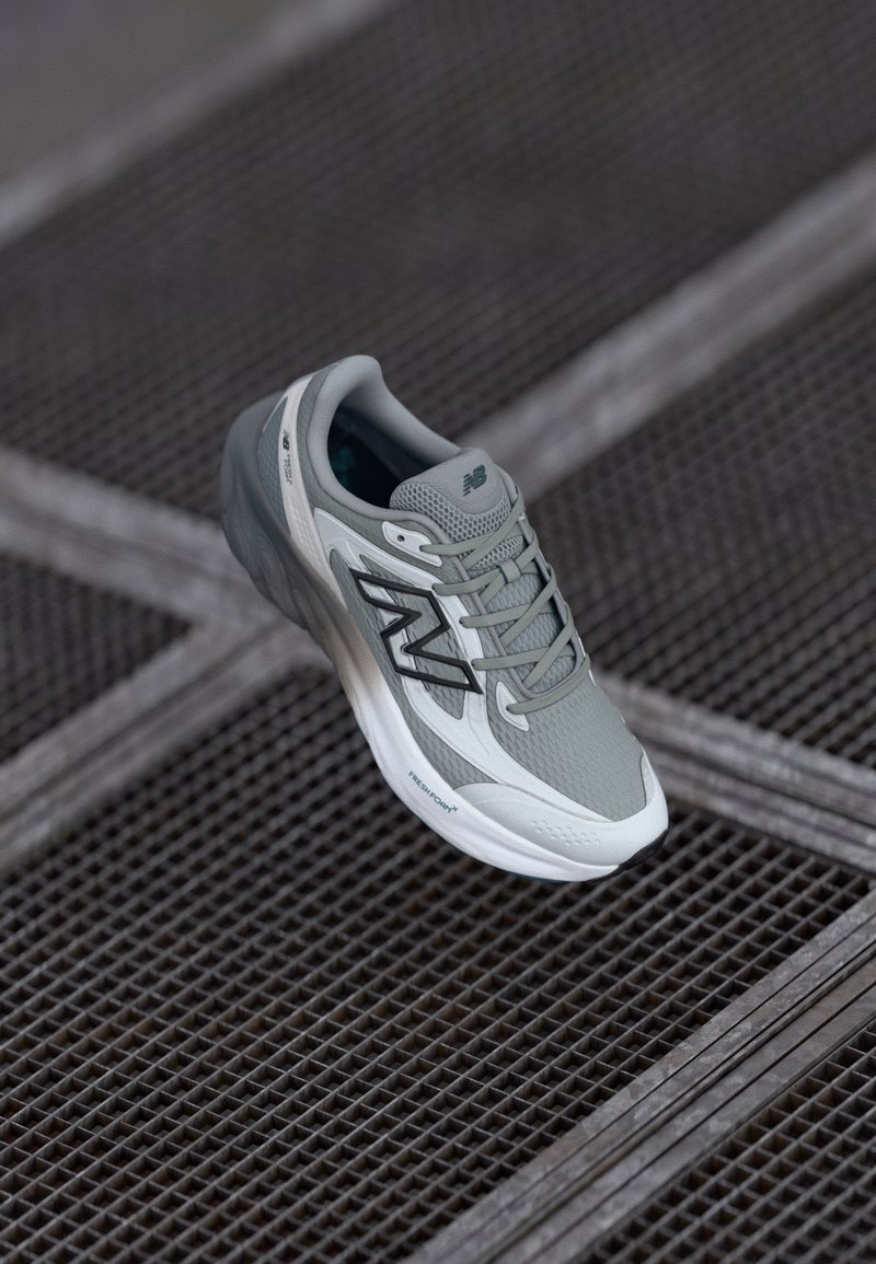 Jasnoszary but do biegania z siateczkową cholewką, wyściółką podeszwy i czarnymi akcentami logo. Charakteryzuje się smukłym designem i teksturowanymi detalami.