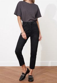 Camiseta de algodón gris, jeans negros de cintura alta y mocasines negros con detalle de cadena. Texturas suaves, ajuste relajado, diseño clásico.