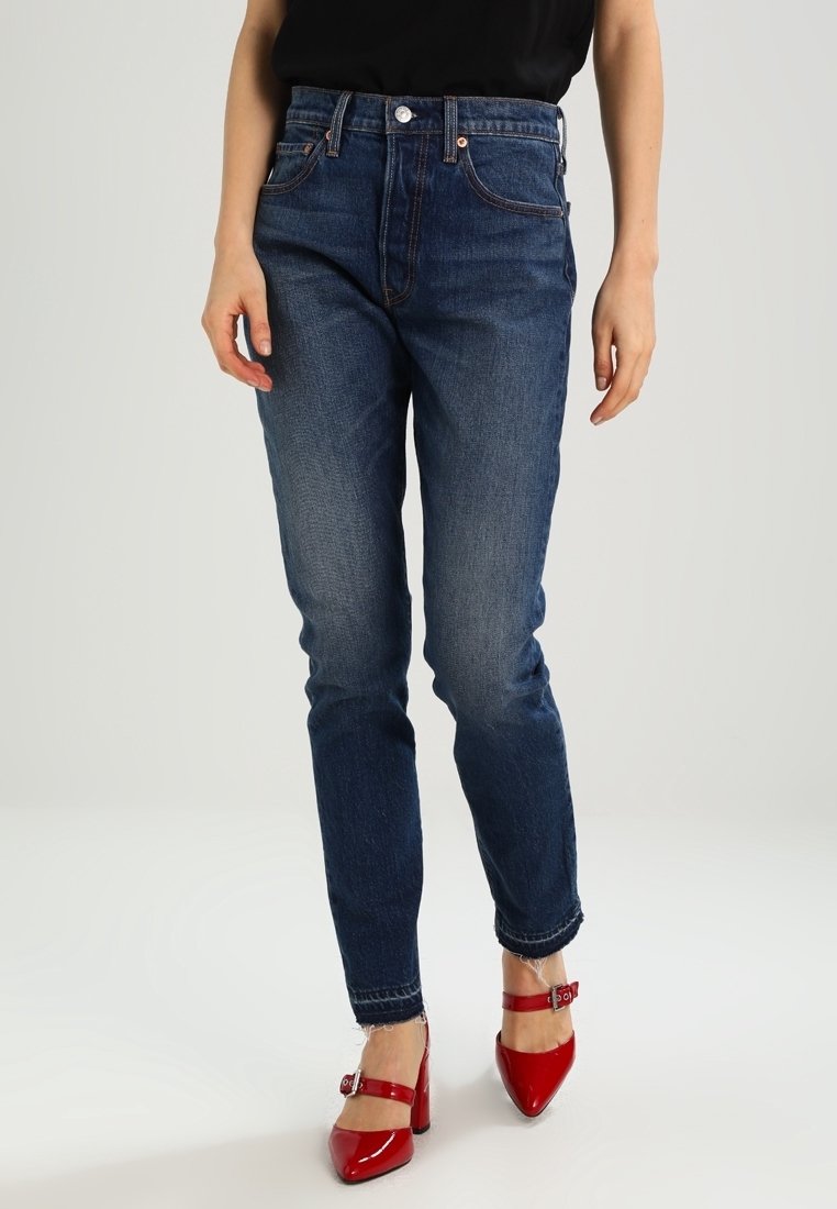 Jean en denim bleu foncé à coupe droite, cinq poches, finition délavée, associé à des talons en cuir verni rouge avec brides à la cheville.