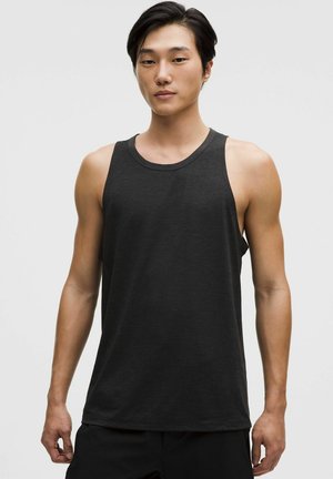 Ung mand med kort sort hår iført en simpel sort ærmeløs atletisk tanktop mod en hvid baggrund.