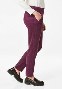 Paarse, zacht aanvoelende broek met een slim fit, voorzien van zijzakken en verticale naden. Gedragen met donkere, stevige loafers.