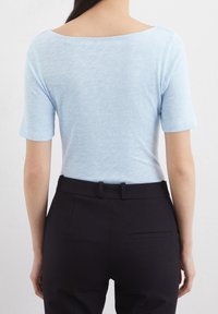 Světle modrý, krátký rukáv top v měkké, texturované pletenině, v kombinaci s černými kalhotami na míru s elegantním pasem a detaily zadní kapsy.