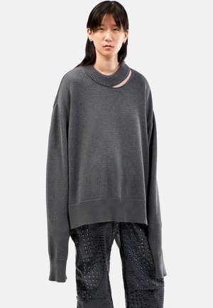 Grijze oversized trui met een geribbelde onderrand en brede halslijn met een uitsnede. Draagt het met gestructureerde zwarte broeken die op krokodillenhuid lijken.