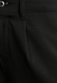 Pantaloni neri in tessuto liscio, dotati di tasca frontale, chiusura a bottone e pieghe sottili, che mettono in mostra un design classico.