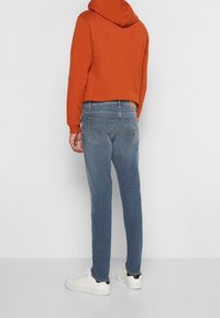 Orange hoodie med avslappnad passform, kombinerad med blekblå skinny jeans och vita sneakers med svart detalj på hälen.