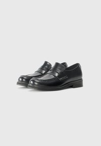Mocassins en cuir noir avec une finition lisse, présentant des détails cousus, un avant légèrement surélevé et un petit talon solide.