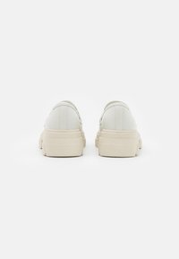 White leather sneakers with a smooth finish, featuring a thick beige rubber sole. Rear view shows a rounded shape and subtle seam detailing.