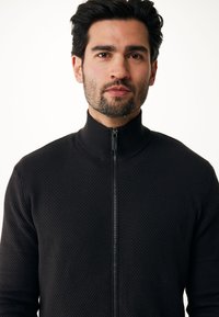 Maglione nero con zip e alto colletto, in tessuto testurizzato e dalla vestibilità aderente. Presenta una zip liscia sul davanti.