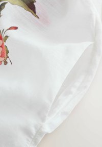 Ziedu raksta audums ar rozā rozēm un zaļām lapām uz baltas, teksturētas fona, ar maigu plūstošību un gludu apdari.