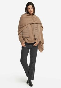 Beige uldtrøje med quiltet frontpanel, parret med mørkegrå jeans. Sorte ankelstøvler. Model draperet i et matchende sjal.