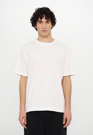 Hvid bomulds t-shirt med korte ærmer, afslappet pasform, rund halsudskæring og glat tekstur. Bæres med sorte bukser, minimalistisk design.