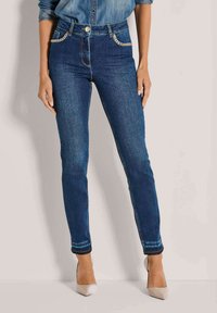 Strakke jeans in donkerblauwe denim met een hoge taille, voorzien van gouden kettingaccenten op de voorkruiszakken en een subtiele vervaging bij de zoom.