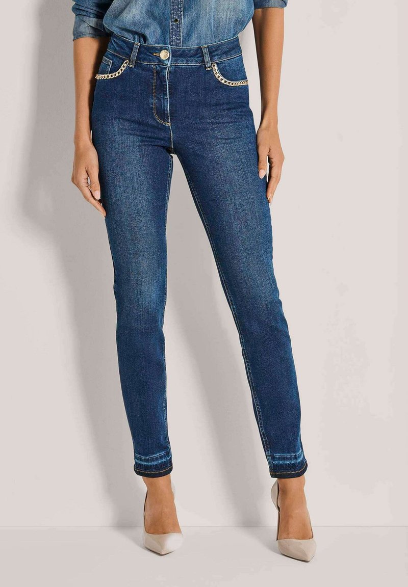 Strakke jeans in donkerblauwe denim met een hoge taille, voorzien van gouden kettingaccenten op de voorkruiszakken en een subtiele vervaging bij de zoom.