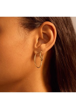 Boucles d'oreilles créoles dorées disponibles en deux tailles, avec une finition lisse et un design circulaire, portées sur l'oreille externe.