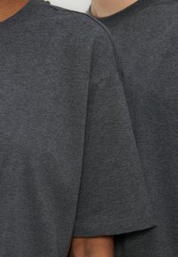 Deux personnes portant des t-shirts unis gris foncé à manches courtes, gros plan sur les épaules et la partie supérieure des bras.