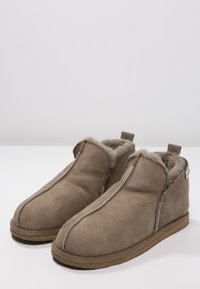 Tan semsket ankelstøvler med et mykt fôr av pels, med kontrastsøm og en flat gummisåle. Slip-on design med minimal hardware.