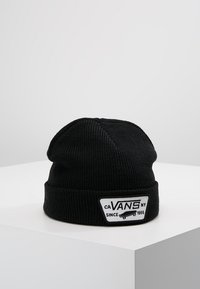 Gorro de punto negro con un puño doblado y un parche rectangular blanco que presenta el texto "CA VANS NY DESDE 1966" y un gráfico de patineta.