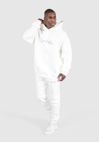Weißer Hoodie mit Fronttasche und besticktem Schriftlogo, kombiniert mit passenden Slim-Fit-Sweatpants. Beide aus weichem Stoff.