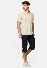 Beige overhemd met korte mouwen, knopen en een kraag, gecombineerd met donkerblauwe cargoshorts met zakken en trekkoorden.