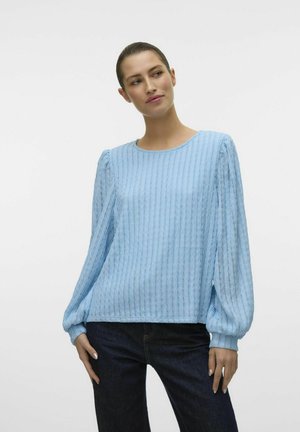 Lys blå langærmet bluse med vertikal ribbet tekstur, rund halsudskæring og sammenrullede ærmekanter. Kombination med mørke denim jeans.