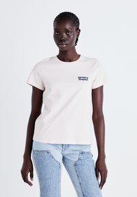 T-shirt en coton rose pâle à manches courtes, avec un patch du logo Levi's bleu marine sur la poitrine gauche. Texture lisse, coupe classique.