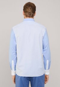 Camisa de manga larga con un cuerpo de color azul claro y rayas verticales blancas, puños blancos y un cuello con botones. Textura suave.