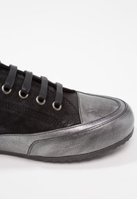 Baskets noires et gris métallisé avec fermeture à lacets, textures en daim et cuir, et détails cousus sur fond blanc.