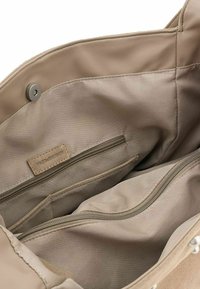 Beige stoffen tas interieur met een gladde textuur, voorzien van twee ritszakken en een merkteken dat aan de zijkant is gestikt.