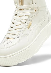 Białe wysokie trampki z gładkiej skóry, złotymi akcentami i grubą, rowkowaną podeszwą. Sznurówki przechodzą przez oczka, zapewniając pewne dopasowanie.