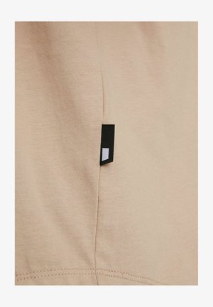 Beige bomullstyg med en slät textur som har en svart etikett på sidan, med en vit rektangulär design.