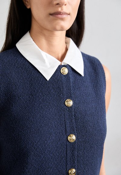 Robe texturée marine avec un col blanc attaché et des boutons dorés. Elle présente un design ajusté et une finition lisse sur le tissu.