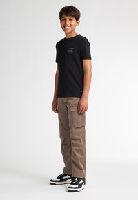 Zwarte katoenen t-shirt met een klein gedrukt ontwerp op de borst, gecombineerd met beige cargobroek met zakken en een relaxed fit. Zwart-witte sneakers.