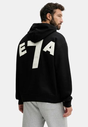 Felpa nera con un grande design bianco "E7A" sulla schiena. Il tessuto sembra morbido con una vestibilità rilassata e un cappuccio regolabile.
