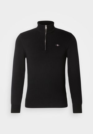 Schwarzer gerippter Strickpullover mit langen Ärmeln, hohem Kragen und silbernem Frontreißverschluss, mit kleinem besticktem Logo auf der linken Brust.