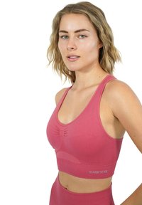 Reggiseno sportivo aderente di un colore rosa uniforme, realizzato in materiale elastico, con scollatura a girocollo, spalline larghe e un delicato dettaglio arricciato.