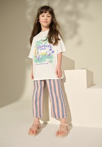 Witte t-shirt met "Beach Club" grafiek, pastelgroen en paars. Roze en blauwe gestreepte denim broek. Tan sandalen met banden.