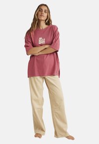 Oversized pink cotton t-shirt with short sleeves and a logo print, paired with beige corduroy wide-leg pants. Soft texture and relaxed fit.