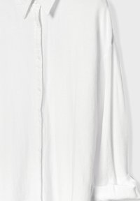 Bijela košulja s dugim rukavima, gumbima, klasičnim ovratnikom, mekane tkanine i blago širokog kroja.