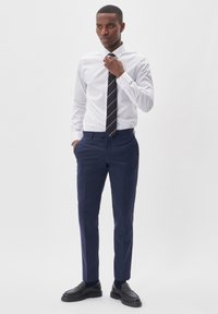 Vit långärmad skjorta, marinblå slips med vita ränder, marinblå kostymbyxor och svarta loafers. Mjukt tyg med skräddarsydd passform och modern design.