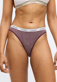 Bordo Calvin Klein bikini kelnaitės su raštuotu dizainu, pasižyminčios balta prekės ženklo juosta ir lygiu audinio tekstūra.