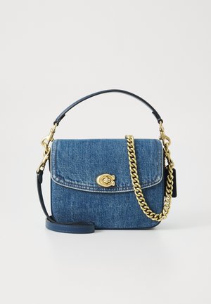 Bolso de mezclilla azul con cierre de solapa, cierre giratorio dorado, asa superior de cuero negro y correa decorativa de cadena dorada sobre fondo blanco.