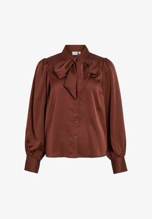 Blusa in satin marrone con colletto alto, dettaglio a fiocco oversize nella scollatura, chiusura con bottoni e maniche lunghe a sbuffo con polsini elasticizzati.