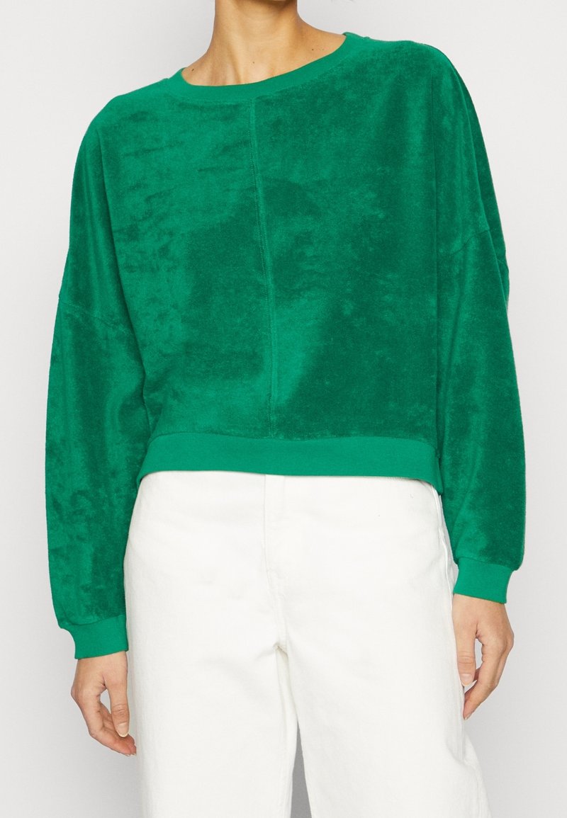 Zelená zkrácená mikina vyrobená z měkké, texturované tkaniny. Má dlouhé rukávy a kulatý výstřih, s jednolitou barvou po celém povrchu.