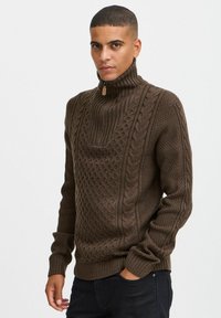 Suéter marrón de punto con cuello alto, que presenta patrones de trenzado texturizados, puños acanalados y un detalle de media cremallera en el cuello.