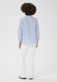 Blusa azzurro chiaro a maniche lunghe con maniche arricciate, abbinata a pantaloni bianchi a palazzo e tacchi a fantasia. Collo semplice e vestibilità rilassata.